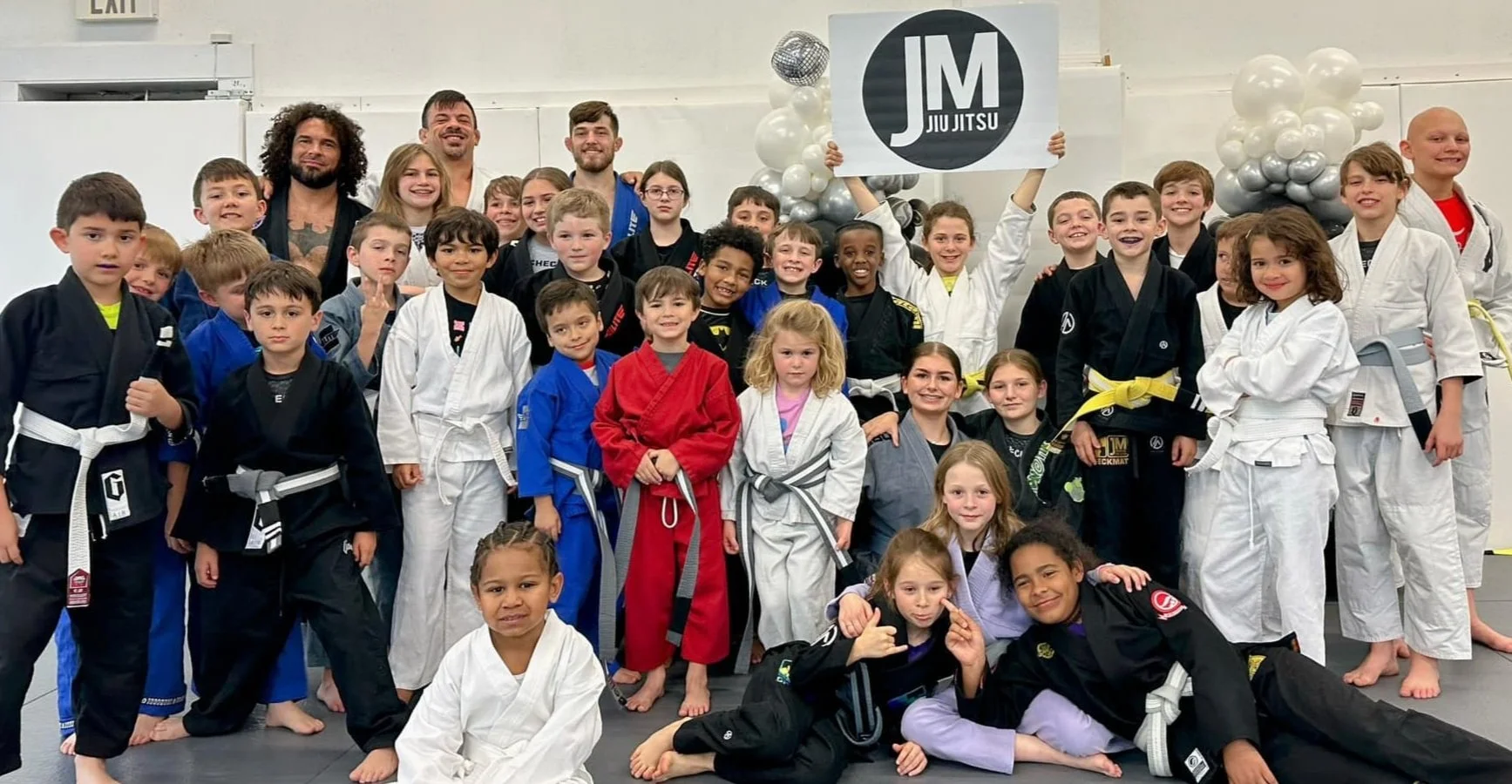 The kids class at JM Modern Jiu Jitsu holding the academy sign